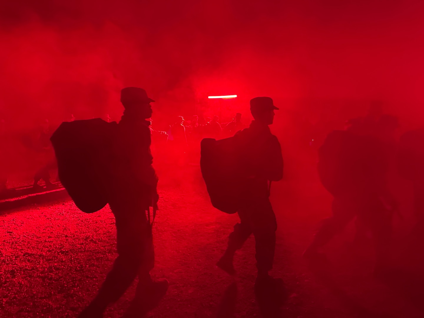 Trainees carry deployment bags under the red light of PACER FORGE