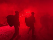 Trainees carry deployment bags under the red light of PACER FORGE