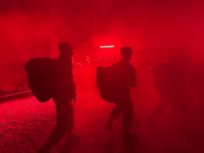 Trainees carry deployment bags under the red light of PACER FORGE