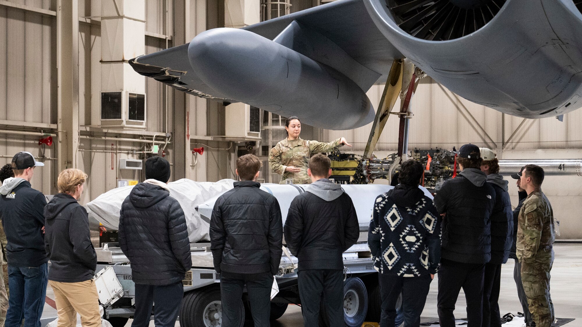 A member of the 5th Maintenance Group presents atop a munition loading trailer to Minot State University Track & Field Team students at Minot Air Force Base, North Dakota, March 4, 2025. Many of the students had prior knowledge of the Air Force’s presence but were not educated on the greater mission of the base. (U.S. Air Force photo by Senior Airman Kendra A. Ransum)