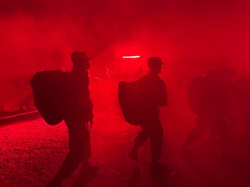 Trainees carry deployment bags under the red light of PACER FORGE