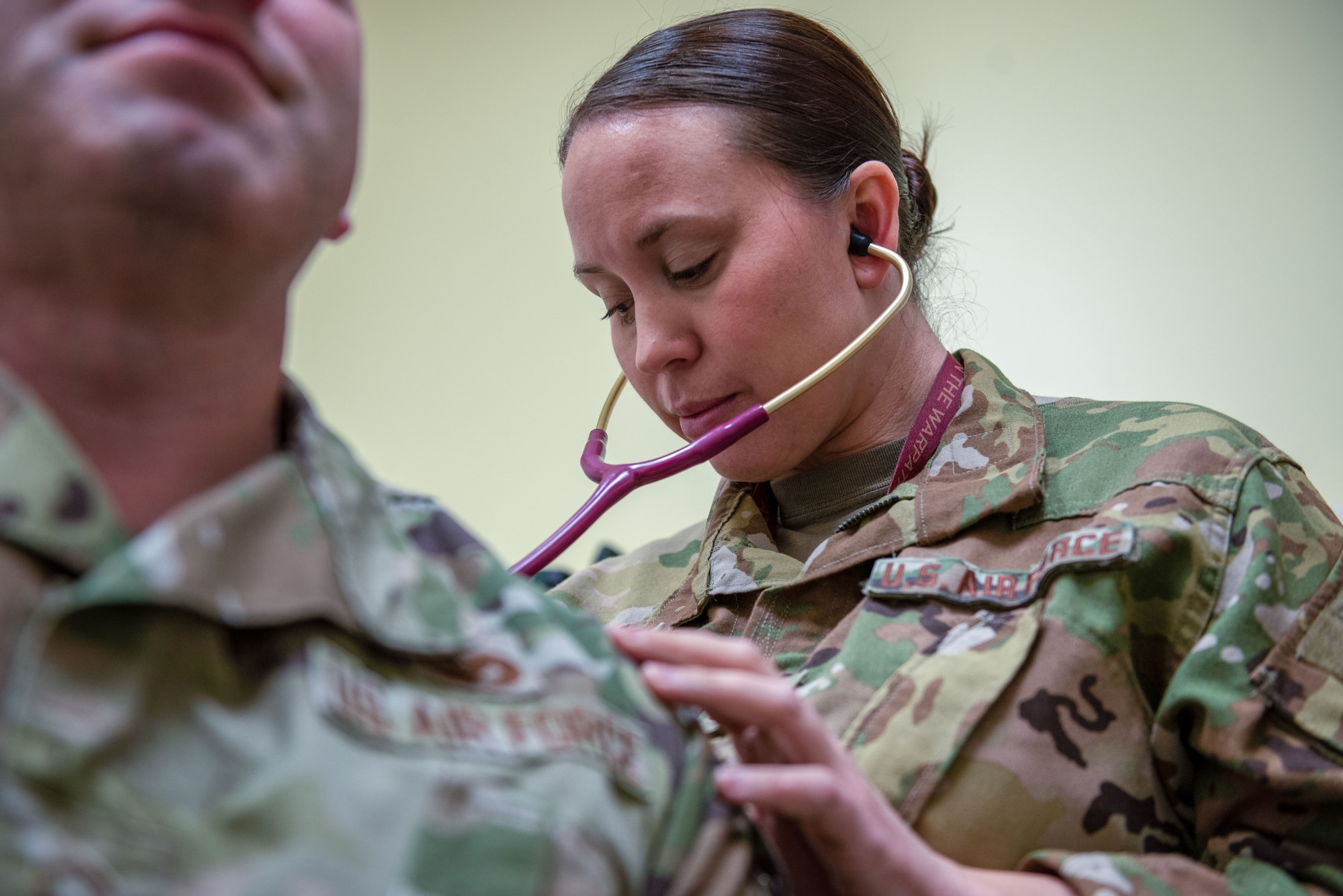 A woman in a military uniform wearing a stethoscope listens to a person's heartbeat.