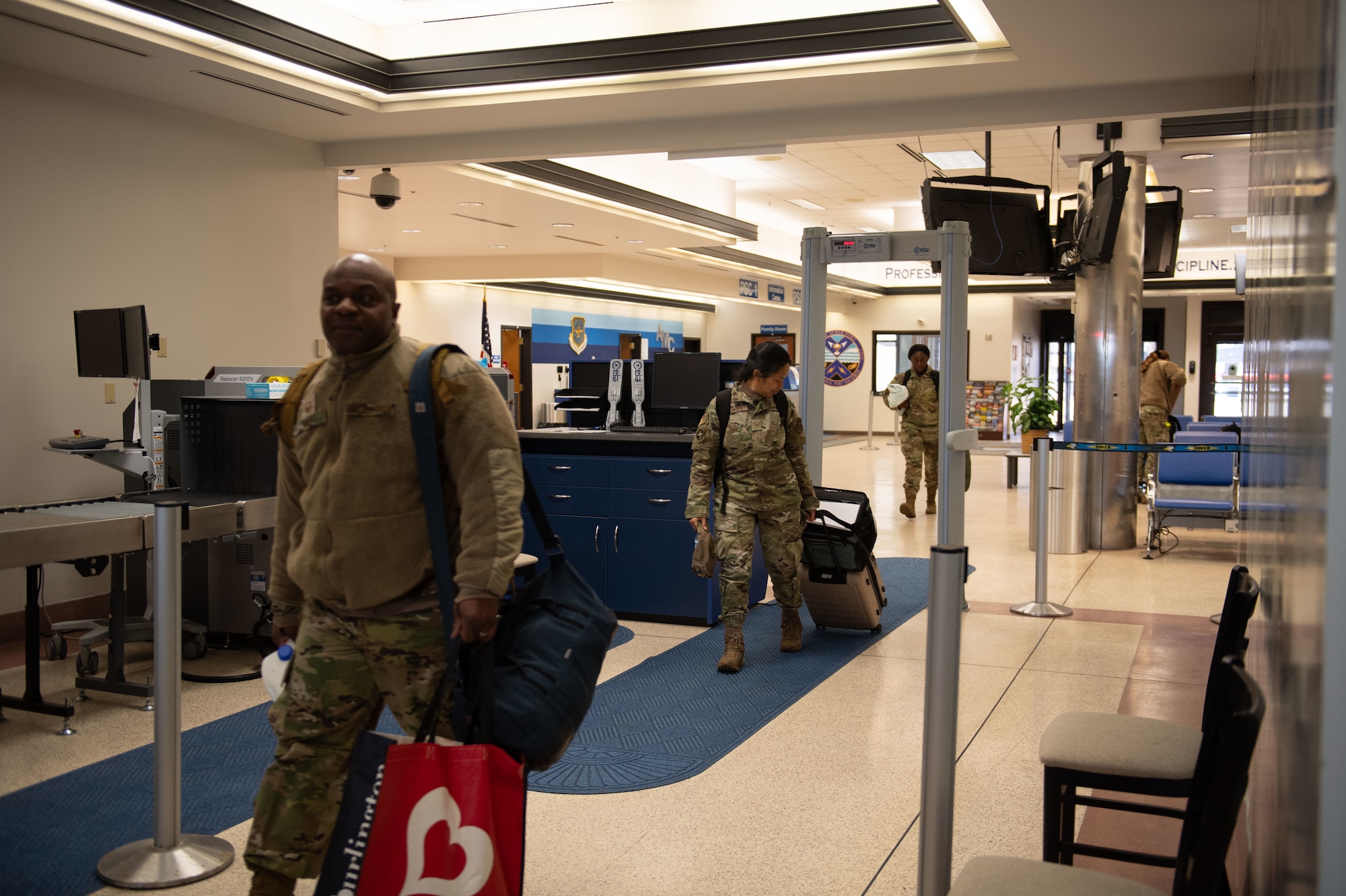 Airmen from the 512th Maintenance and Aircraft Maintenance Squadrons and 712th Aircraft Maintenance Squadron pass through a walk-through metal detector to a waiting bus at the Passenger Terminal at Dover Air Force Base, Delaware, Mar. 8, 2025.  At the 436th Aerial Port Squadron Passenger Terminal, active duty, reserve, guard, disabled veterans, retirees and their dependents can travel overseas on the C-5M Super Galaxy and the C-17 Globemaster III, at a low cost. (U.S. Air Force photo by Airman 1st Class Liberty Matthews)