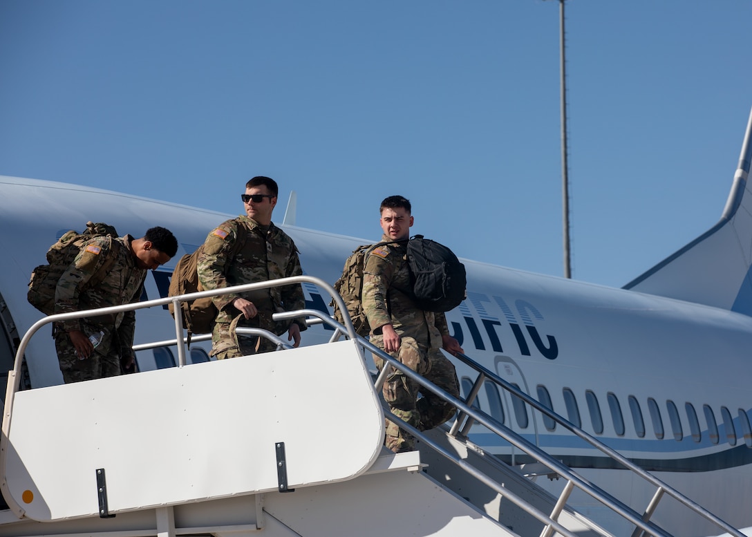 Soldiers exit an aircraft against a blue sky.
