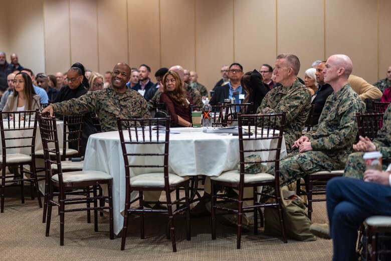 Marines in the audience, sitting at round tables as they listen to the speaker off-screen.