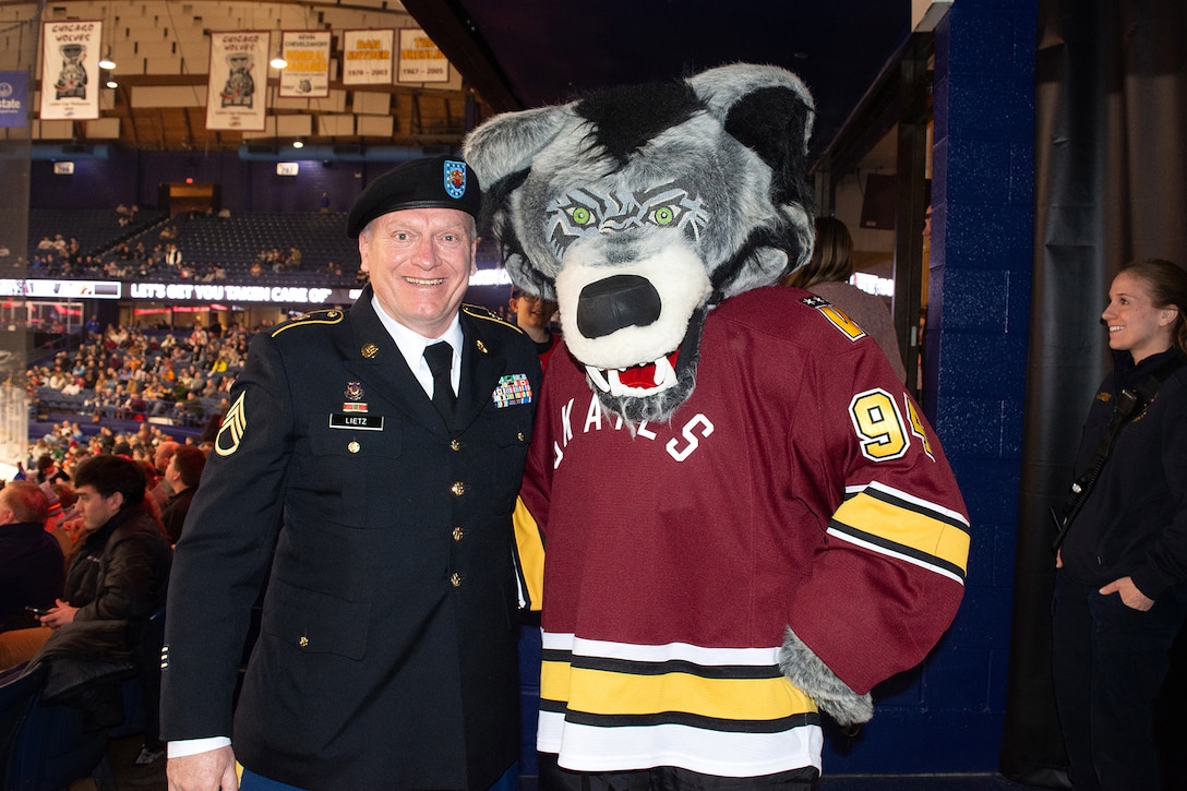 Staff Sgt. David Lietz, 85th U.S. Army Reserve Support Command, public affairs noncommissioned officer, pauses for a photo with Skates, the Chicago Wolves mascot, during a military appreciation event at All-State Arena, March 8, 2025.