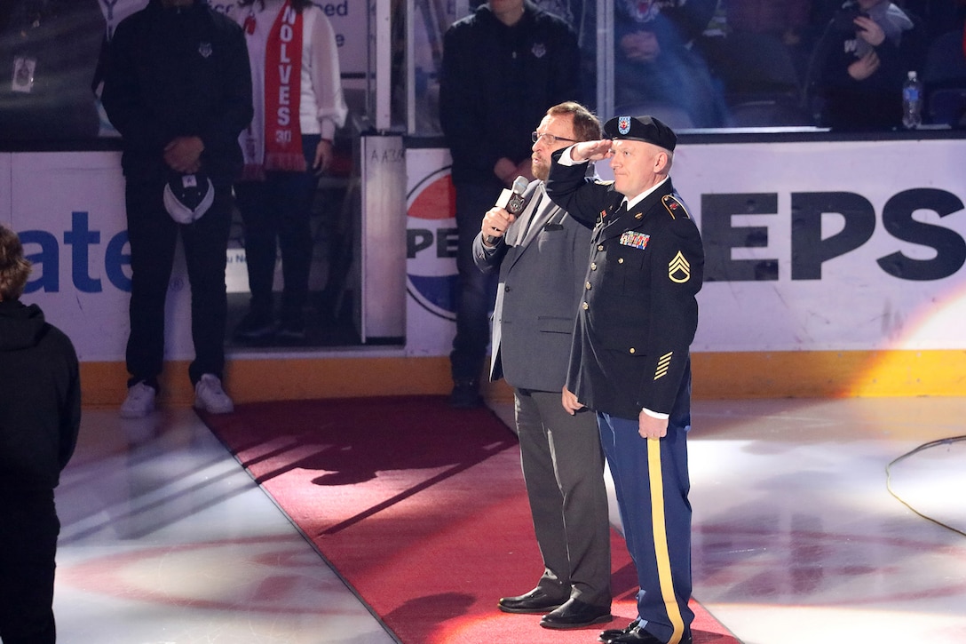 Staff Sgt. David Lietz, 85th U.S. Army Reserve Support Command, public affairs noncommissioned officer, salutes the American flag while Wayne Messmer, professional singer, broadcaster, sings the National Anthem at All-State Arena, March 8, 2025.