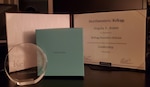 An Award certificate mentioning Angela D. Jones as the Kellog Executive scholar and a glass trophy with a gift.