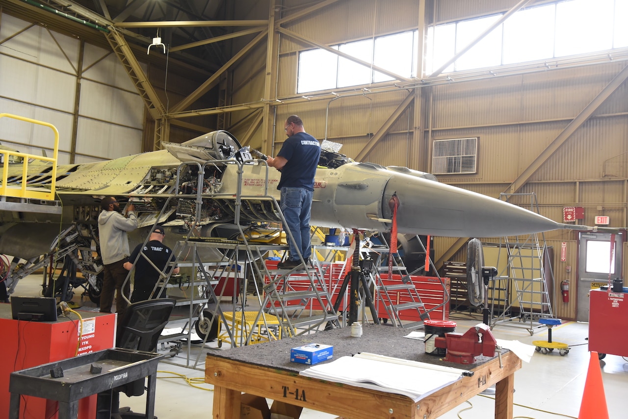 Workers work on an airplane in a hangar facility.