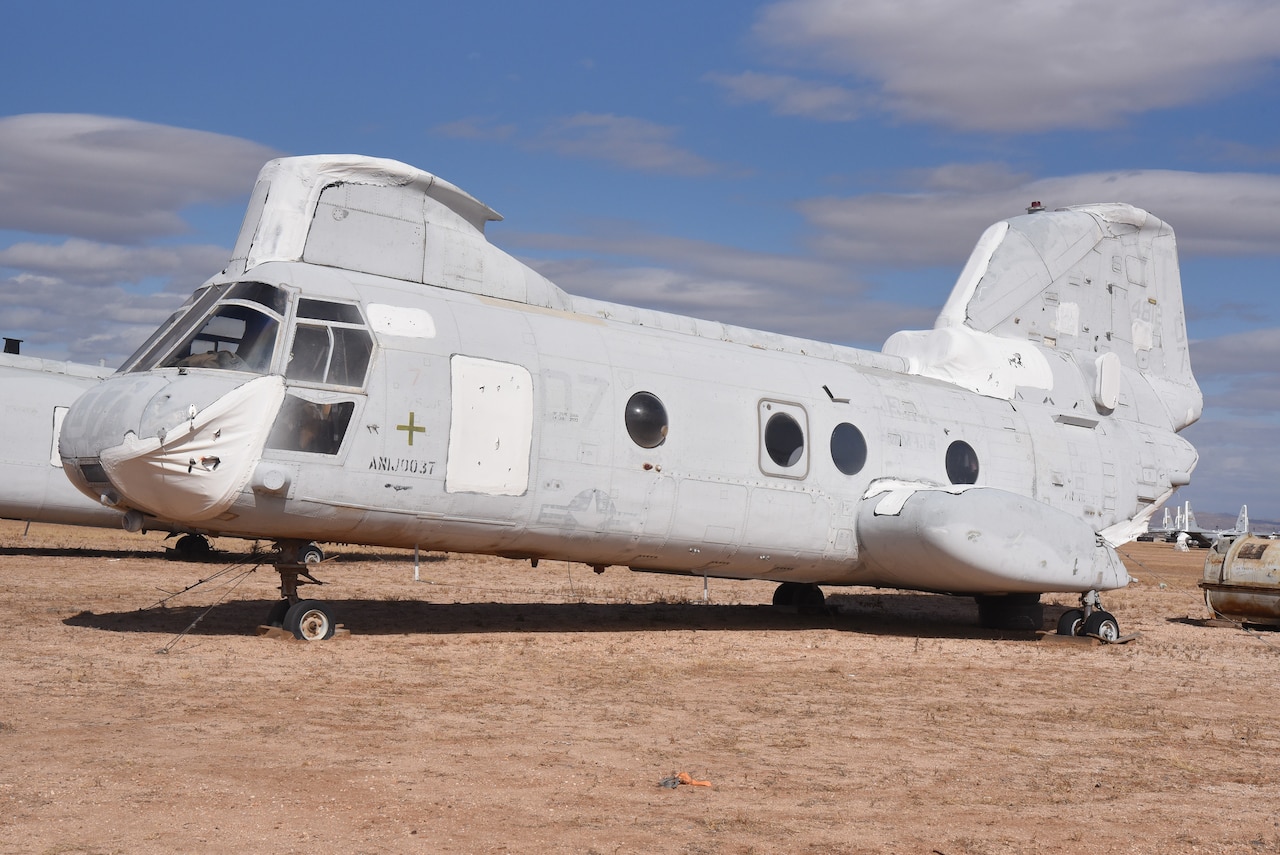 A large helicopter is parked in the desert without its rotor blades.