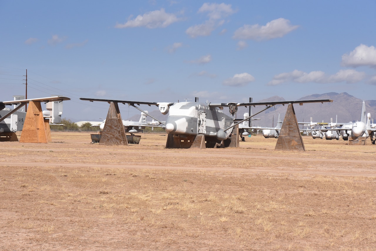 An aircraft stored on wooden structures is parked in the desert alongside other aircraft.