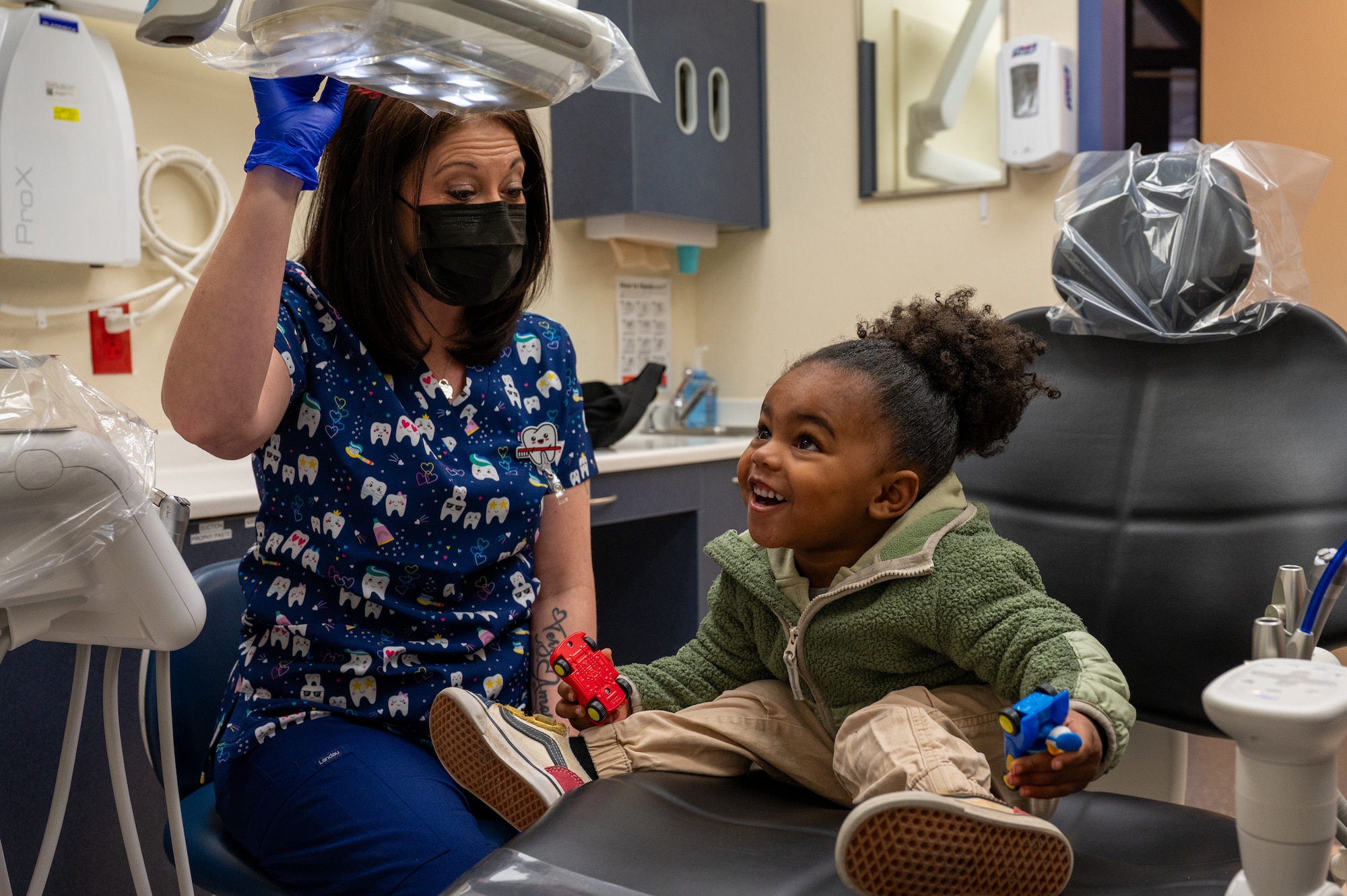 Child looks up at the overhead light with amazement as the dental technician waves her hand under it to turn it on and off.