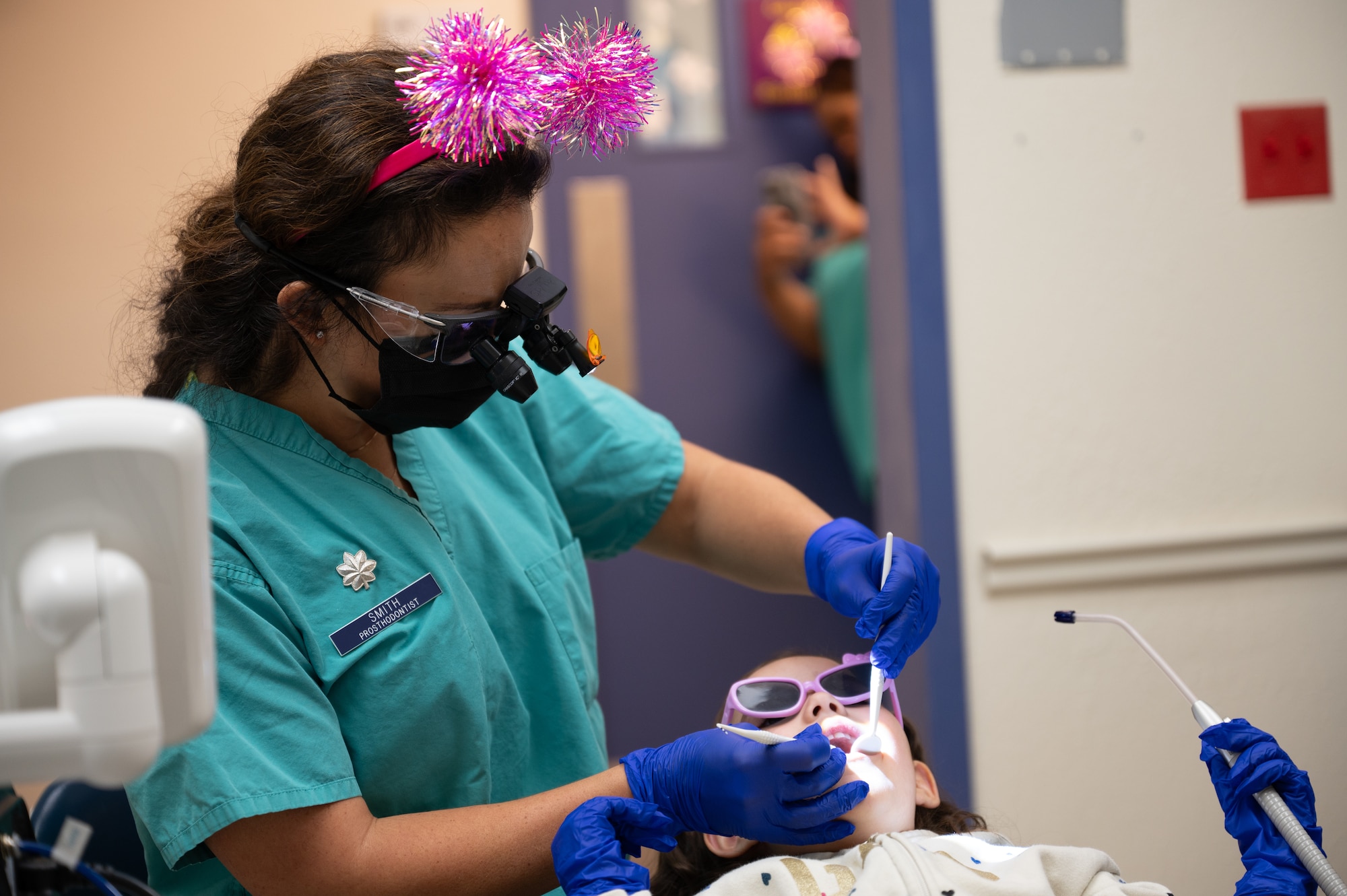 U.S. Air Force Lt. Col. Nicole Smith a prosthodontist, examines a young patient’s teeth using a dental mirror. The child held the suction device.