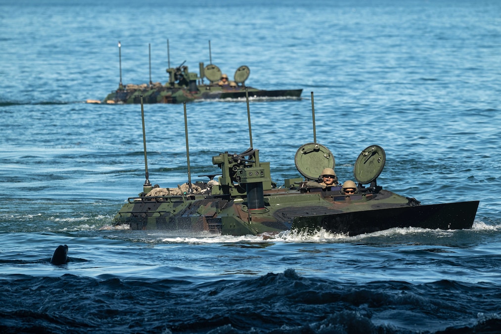 Marines maneuver two amphibious vehicles in the ocean on a sunny day.