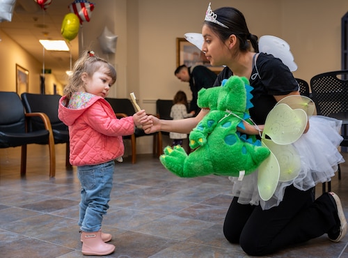 A child curiously examines a toothbrush being handed to her by a woman dressed as the tooth fairy.