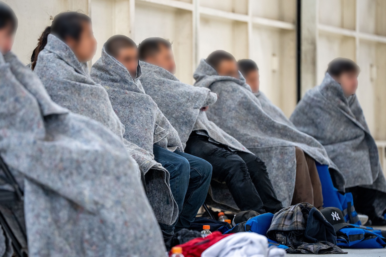 Aliens, bundled in blankets for warmth, sit in the hangar at Sector San Diego.