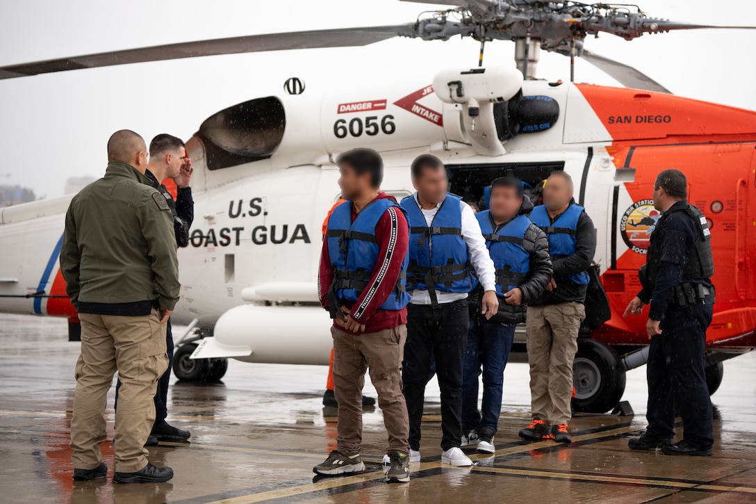 Aliens disembark from a Jayhawk MH-60 as U.S. Coast Guard and Customs and Border Protection personnel standby.