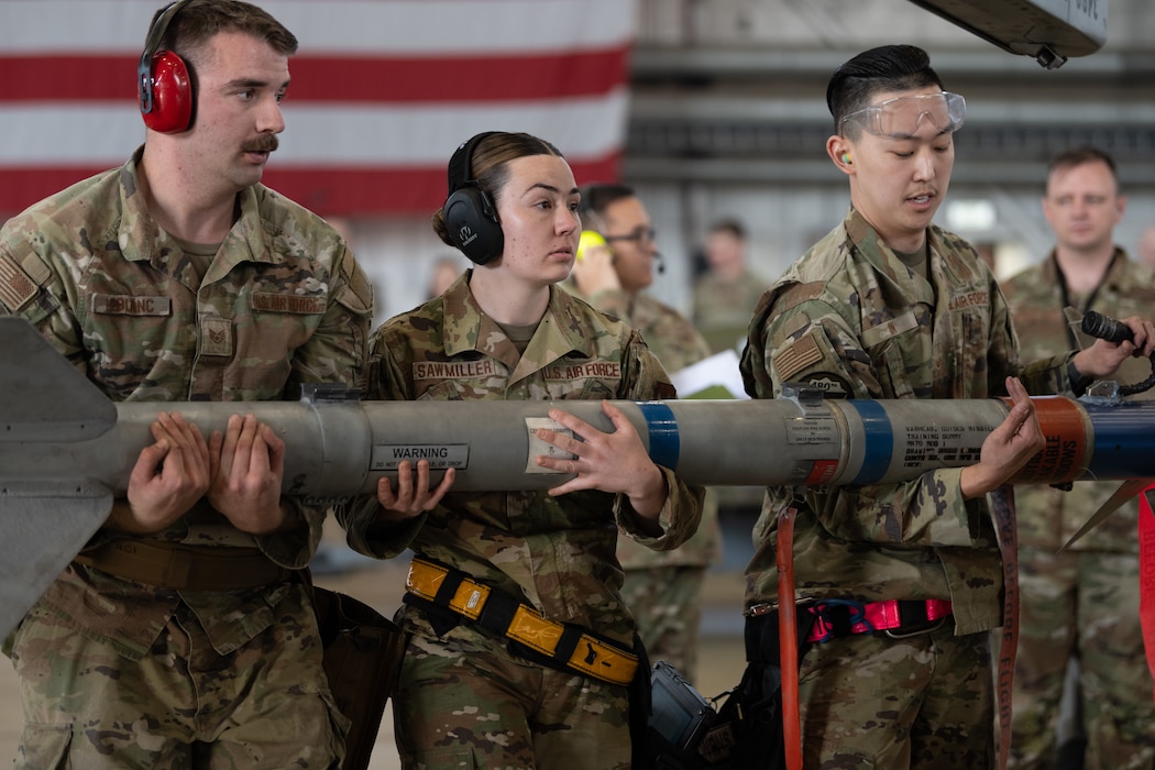 Three U.S. Air Force Airmen carry a munition.