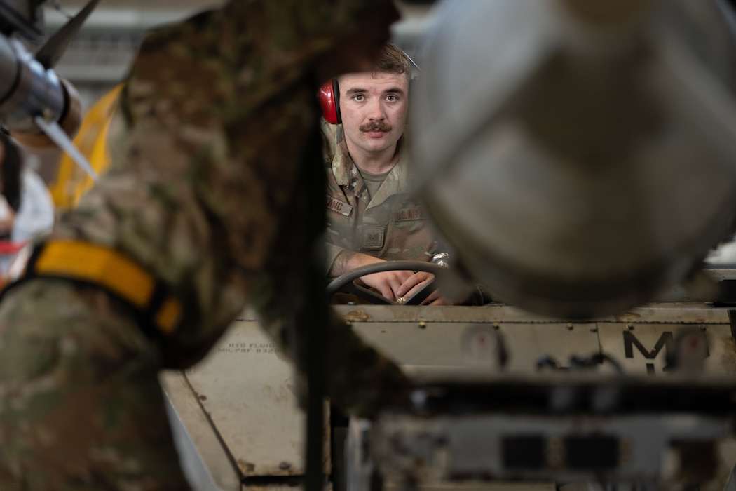 A U.S. Air Force Airman loads a munition onto an aircraft with a vehicle.