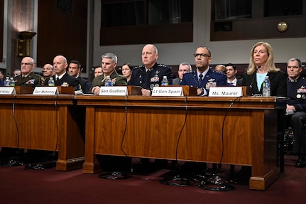 Military leaders and one civilian sit at a long table behind name placards and microphones