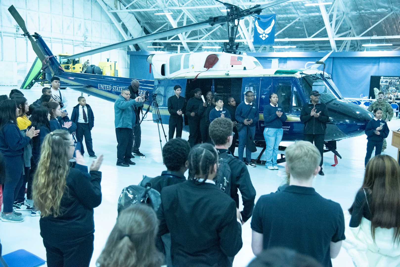 Local high school students gather to listen to closing remarks by Treniece Terry, Defense Threat Reduction Agency technical engagements program manager, during the Seventh Annual Aerospace Summit at Joint Base Andrews, Md., March 4, 2025. The 1st Helicopter Squadron provided a UH-1N Huey for static display, enabling students the opportunity to view the helicopter close-up. (U.S. Air Force photo by Patrick Griffith)