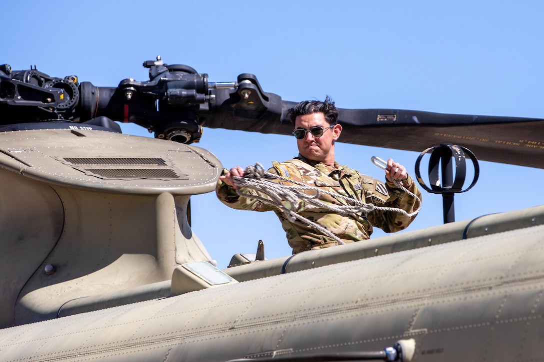 A soldier throws rope over the top of a helicopter during a clear day.