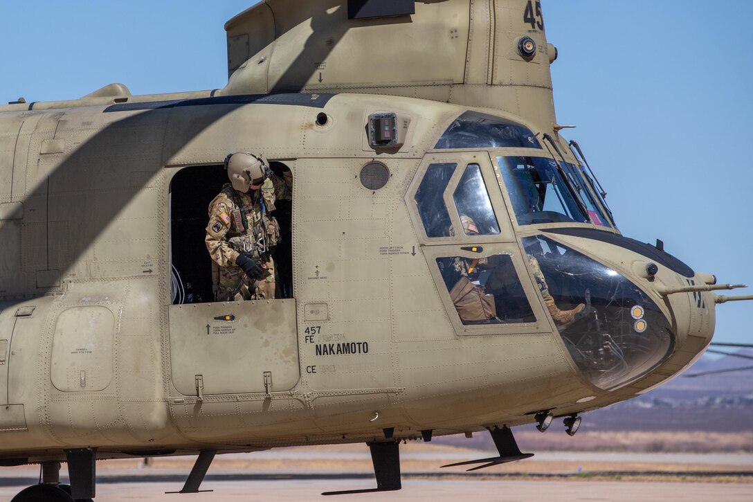 A soldier looks out of a helicopter flying slightly above the ground.