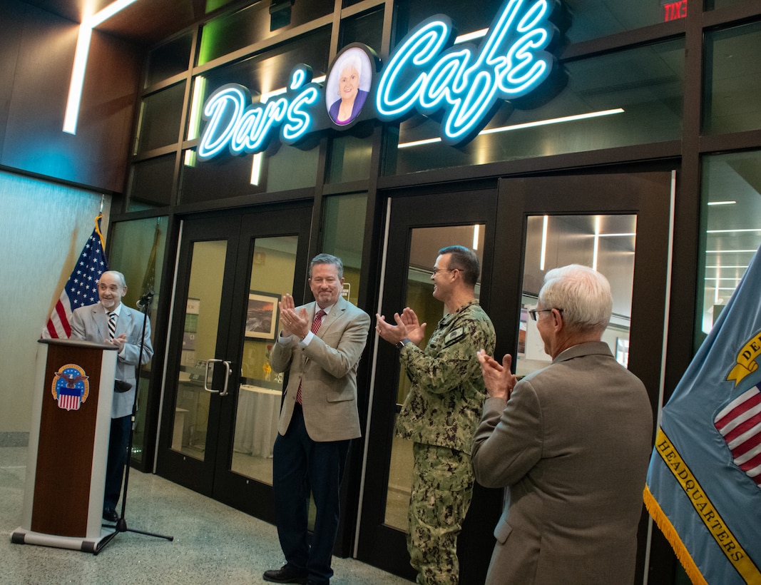 Four men stand applauding under a neon-lit sign that says 'Dar's Cafe'.