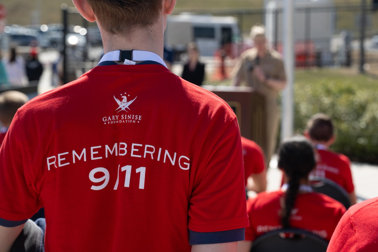A student stands to listen to a man speak. The student’s shirt reads "Remembering 9/11."