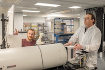 Two people work on pieces of equipment. Both look towards a computer screen.