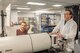 Two people work on pieces of equipment. Both look towards a computer screen.