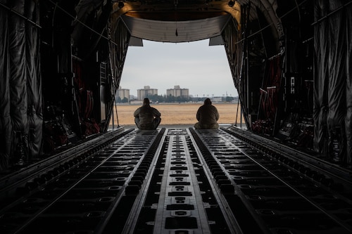 Two Airmen sitting at the end of the cargo bay of a C-130
