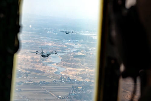 Two C-130J aircraft flying above farmland