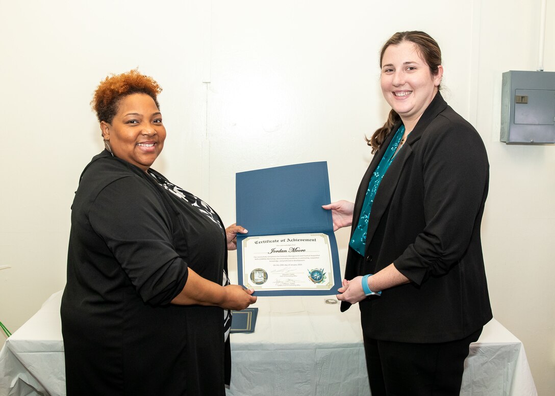 Norfolk Naval Shipyard Contracting Department Business Operation Division Head Donyette Rodgers (left) presents the Contracts Management & Practical Acquisition Skills (CMPAS) Workshop completion certificate to Contract Specialist Jordan Moore. Moore was one of nine to attend the inaugural 13-week program, which consisted of over 100 hours of academic instruction and 50 hours of hands-on training through mock procurements.