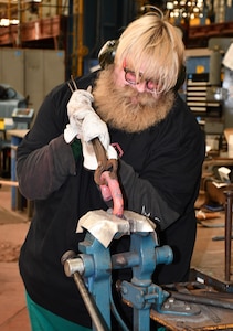Norfolk Naval Shipyard Metal Forging Shop (Shop 11F) Metal Forger Christopher “Toad” Kanash originally wanted to be an actor, then decided to change his degree to management. His father recommended that he apply for a position at the shipyard until he figured things out. “I wanted to work with Morale, Welfare and Recreation (MWR), but there wasn’t a position available at the time, so I decided to join the apprentice program,” said Kanash. “I love heat and working with fire to create something from scratch. I’ve been doing this for 10 years now and I still love it as much as I did when I first started.”