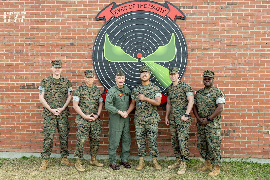 U.S. Marine Corps Cpl. Steven Akridge (Right Center), from Virginia, a tactical air defense controller with Marine Air Control Squadron (MACS) 2, was awarded with a cowbell from Maj. Gen. William H. Swan, from Wisconsin, commanding general, 2nd Marine Aircraft Wing (MAW), alongside his staff at Marine Corps Air Station Cherry Point, North Carolina, March 13, 2025. Cpl. Akridge was awarded the 2nd MAW commanding general's cowbell award for his outstanding performance as a datalink coordinator with Combined Joint Task Force – Horn of Africa. (U.S. Marine Corps photo by Pfc. Gavin Kulczewski)