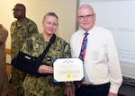 JOINT BASE SAN ANTONIO-FORT SAM HOUSTON – (March 13, 2025) – Dr. John Simecek, director, Craniofacial Health and Restorative Medicine (CHRM), was awarded the Civilian Service Commendation Medal by Naval Medical Research Unit (NAMRU) San Antonio Commanding Officer Capt. Jennifer Buechel, Nurse Corps, during an All Hands Meeting held at the Battlefield Health and Trauma Research Institute. Simecek, a retired Naval dentist, joined the Navy in 1972 serving for 23 years and retired at the rank of lieutenant commander. He joined NAMRU San Antonio in 2009 and has served as the CHRM director for 11 years. He will be retiring from federal service in the fall and will miss the camaraderie. NAMRU San Antonio is one of eight research laboratories within Naval Medicine Research and Development.  Its mission is to conduct gap driven combat casualty care, craniofacial, and directed energy research to improve survival, operational readiness, and safety of Department of Defense personnel engaged in routine and expeditionary operations. (U.S. Navy photo by Burrell Parmer, NAMRU San Antonio Public Affairs/Released)
