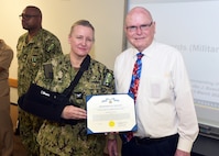 JOINT BASE SAN ANTONIO-FORT SAM HOUSTON – (March 13, 2025) – Dr. John Simecek, director, Craniofacial Health and Restorative Medicine (CHRM), was awarded the Civilian Service Commendation Medal by Naval Medical Research Unit (NAMRU) San Antonio Commanding Officer Capt. Jennifer Buechel, Nurse Corps, during an All Hands Meeting held at the Battlefield Health and Trauma Research Institute. Simecek, a retired Naval dentist, joined the Navy in 1972 serving for 23 years and retired at the rank of lieutenant commander. He joined NAMRU San Antonio in 2009 and has served as the CHRM director for 11 years. He will be retiring from federal service in the fall and will miss the camaraderie. NAMRU San Antonio is one of eight research laboratories within Naval Medicine Research and Development.  Its mission is to conduct gap driven combat casualty care, craniofacial, and directed energy research to improve survival, operational readiness, and safety of Department of Defense personnel engaged in routine and expeditionary operations. (U.S. Navy photo by Burrell Parmer, NAMRU San Antonio Public Affairs/Released)