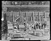 This photograph from August 23, 1905 shows the first granite block being lowered into Dry Dock 3 as naval officers, shipyard leadership, and personnel look on.