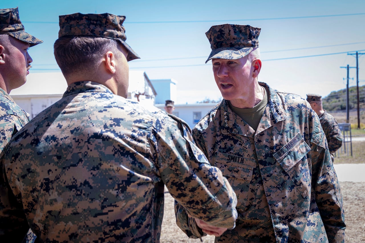 A Marine Corps officer shakes hands with another with others nearby.