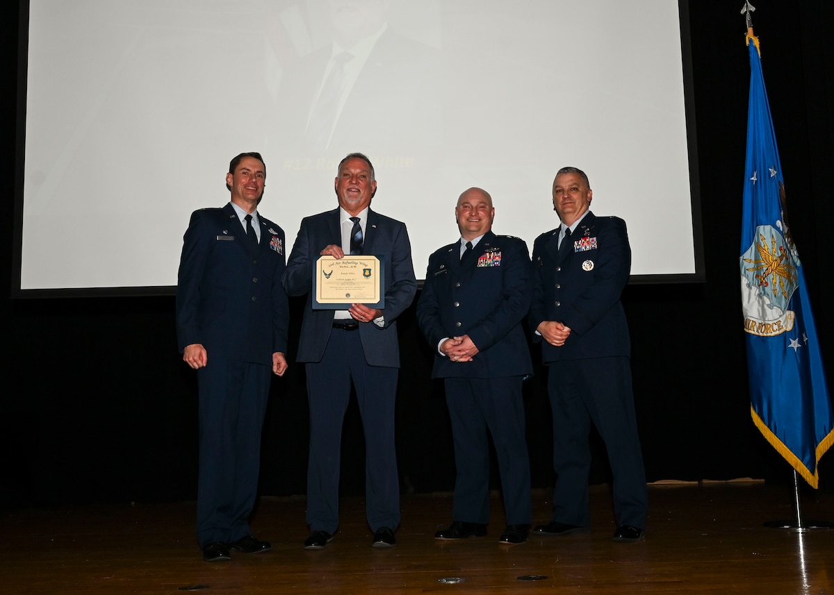 Men in military uniforms and a man in a suit holding a piece of paper pose for a photo.