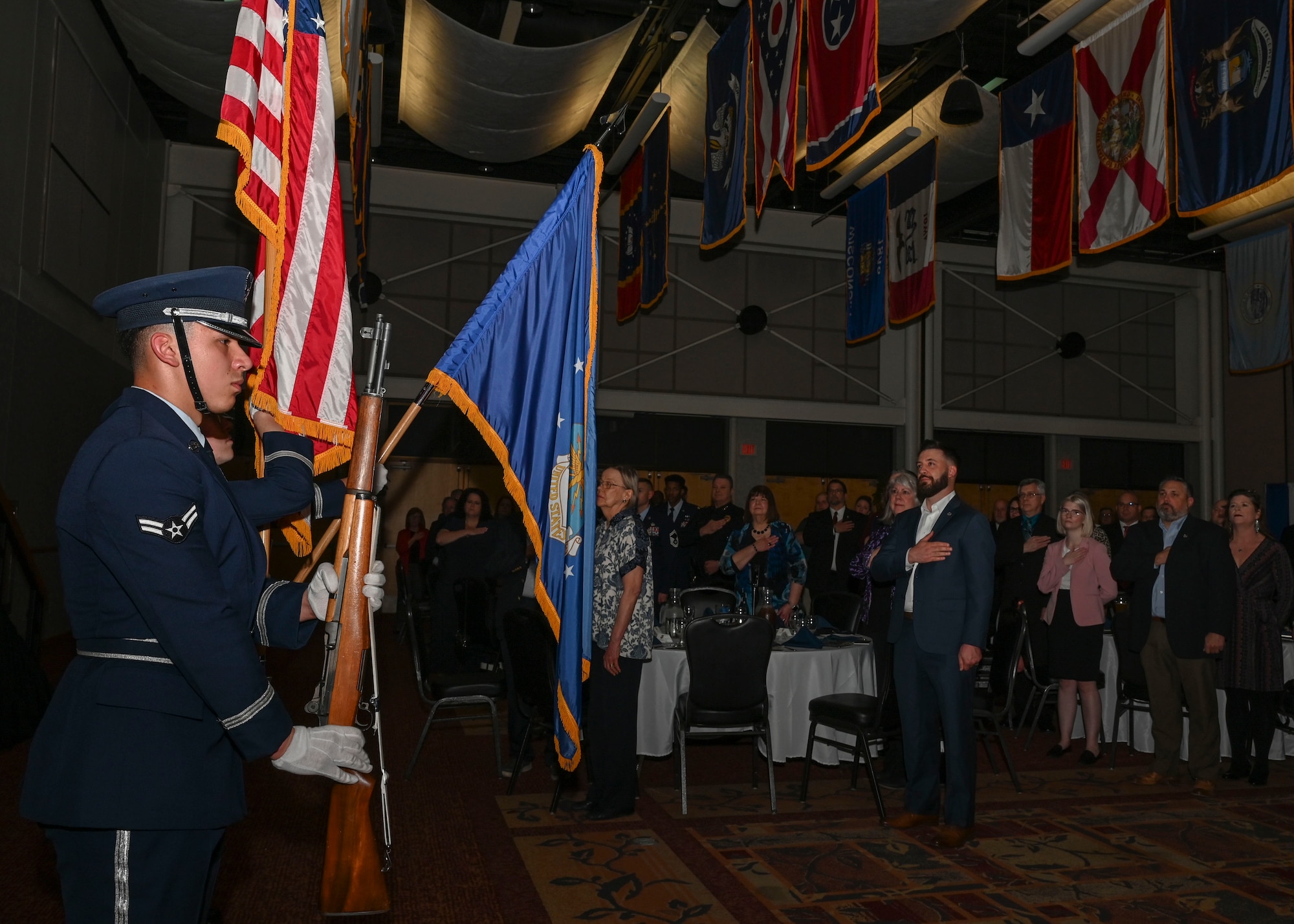People in military dress uniforms fold flags and rifles to present the colors.