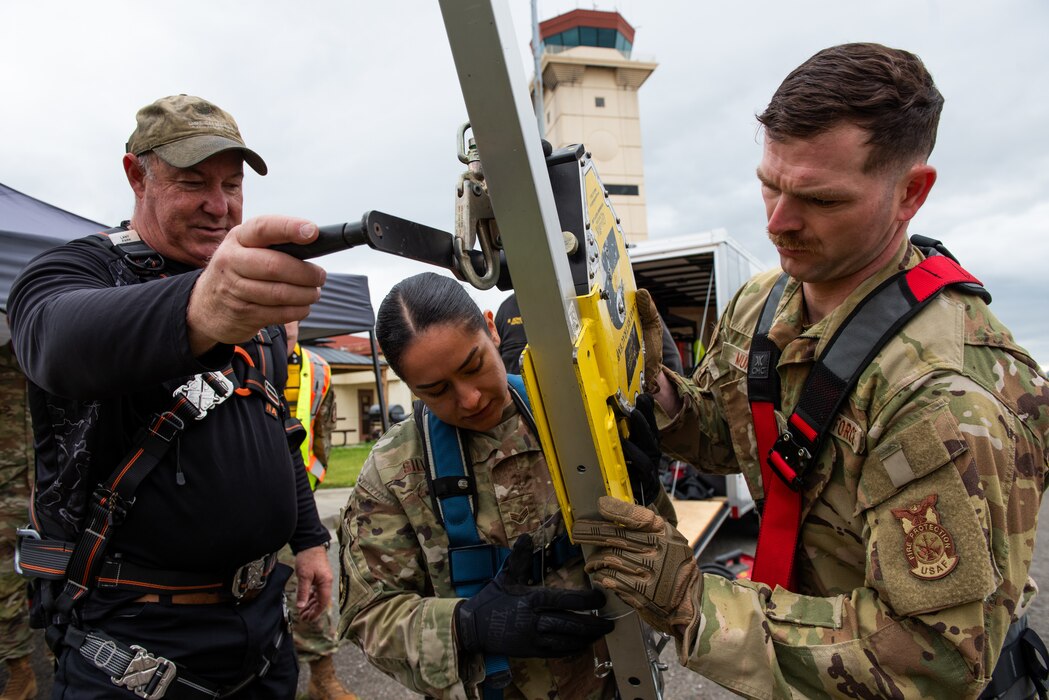 Airmen attach a retractable safety cable to a rescue tripod for confined space safety training