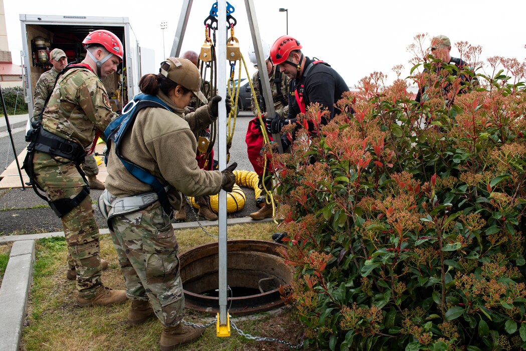 Airmen secure a rescue tripod over a manhole cover