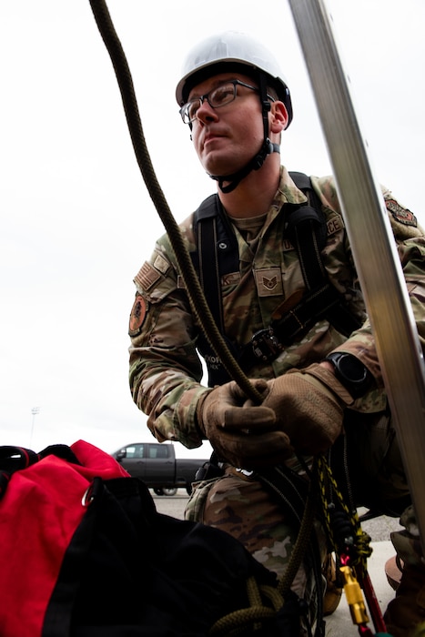 An Airman secures the brake line on a rescue tripod over a manhole cover