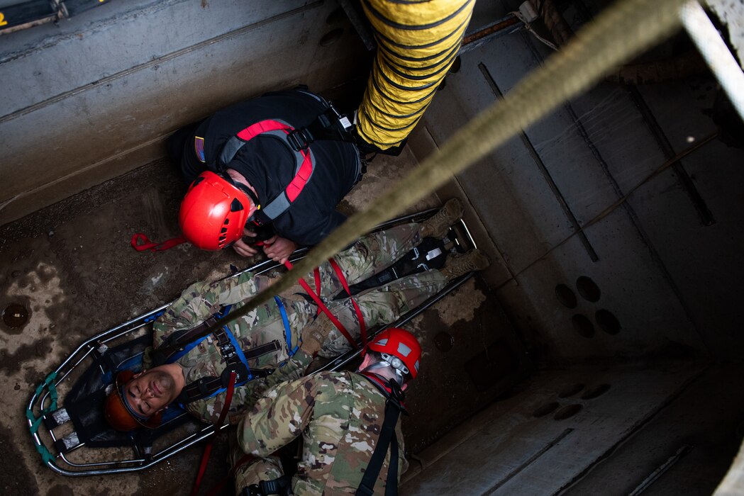 Airmen are performing training in a man hole with a rescue basket