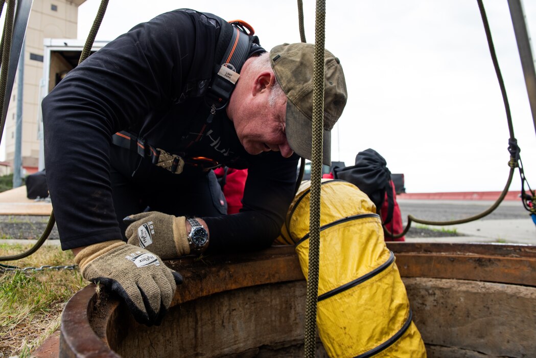 A trainer observes Airman performing training in a man hole