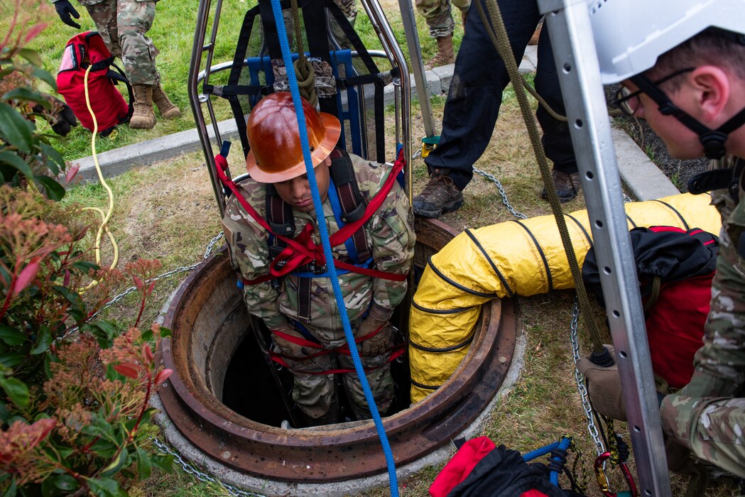 An airman is hoisted from a man hole in a basket for training