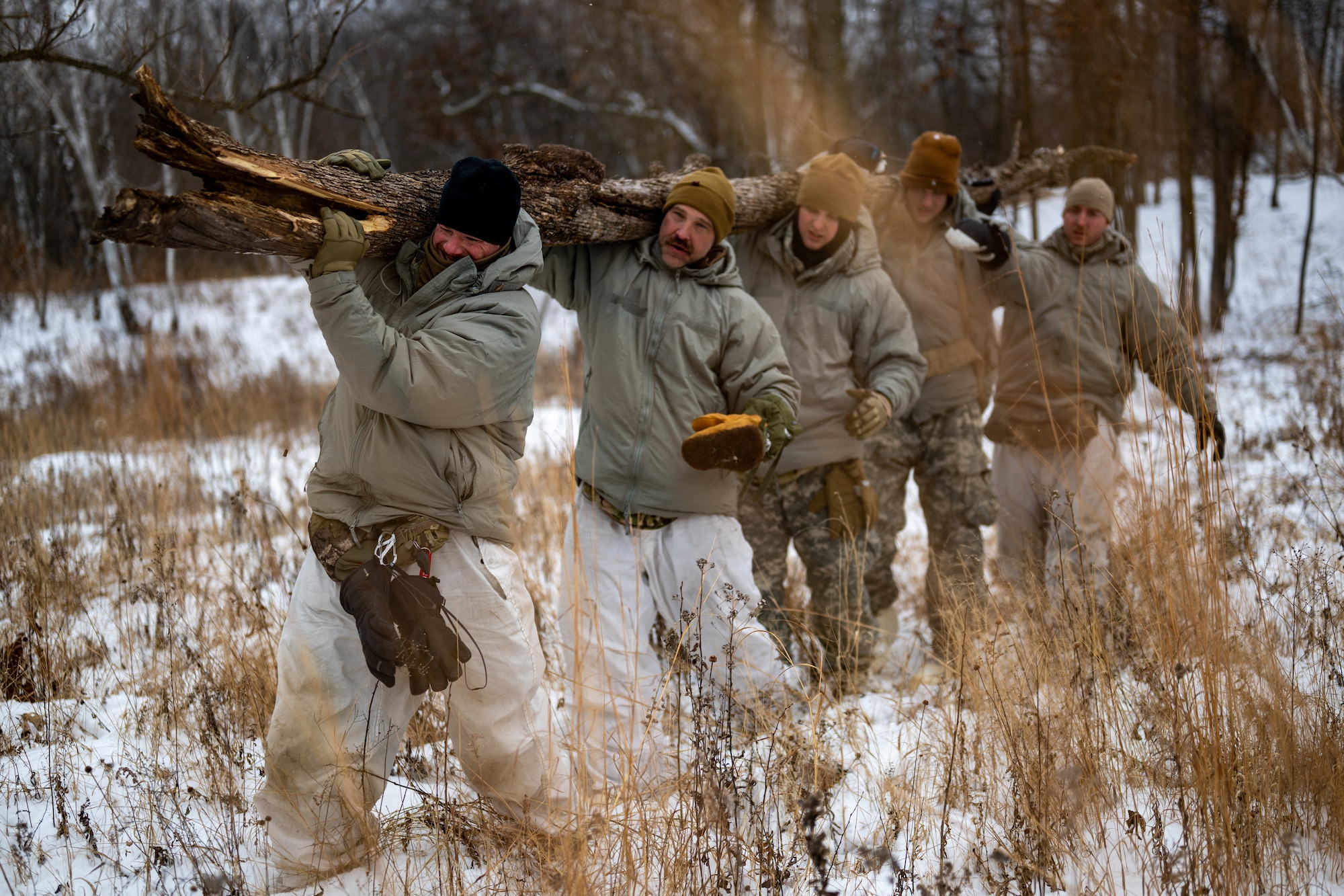 A team of four men carry a large wooden log over their shoulders.