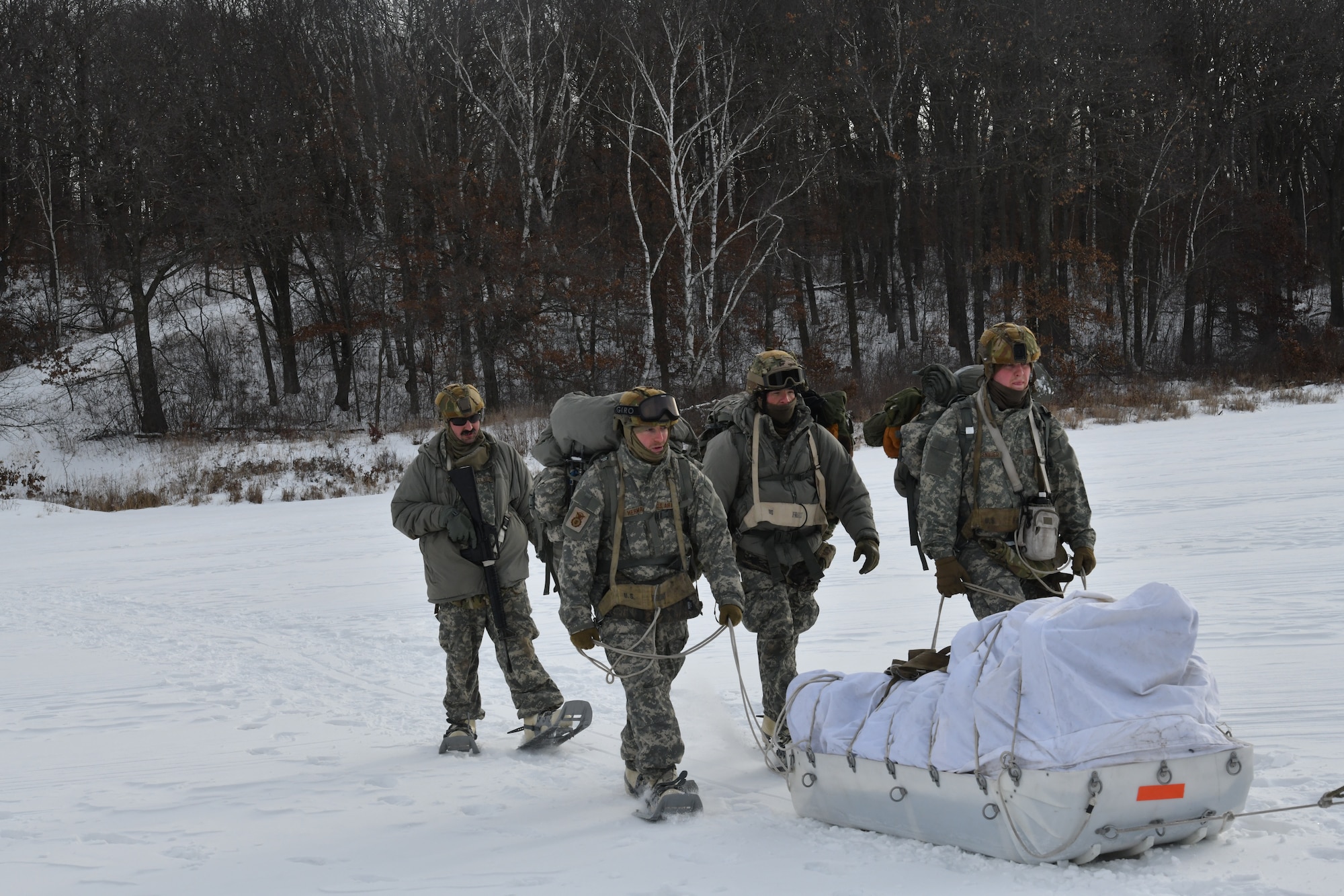Four men walk through the outdoors carrying a large sled with supplies.